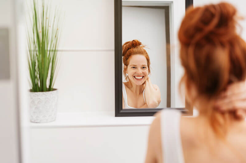 A vibrant woman smiling in the mirror.